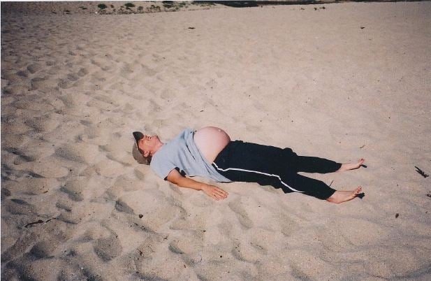 A pregnant woman sunning her tummy at the beach.